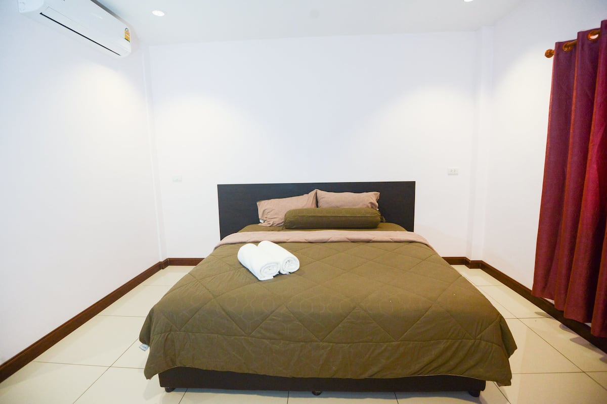 A neatly made bed with a brown quilt, a headboard, and a pair of rolled towels on the bed.