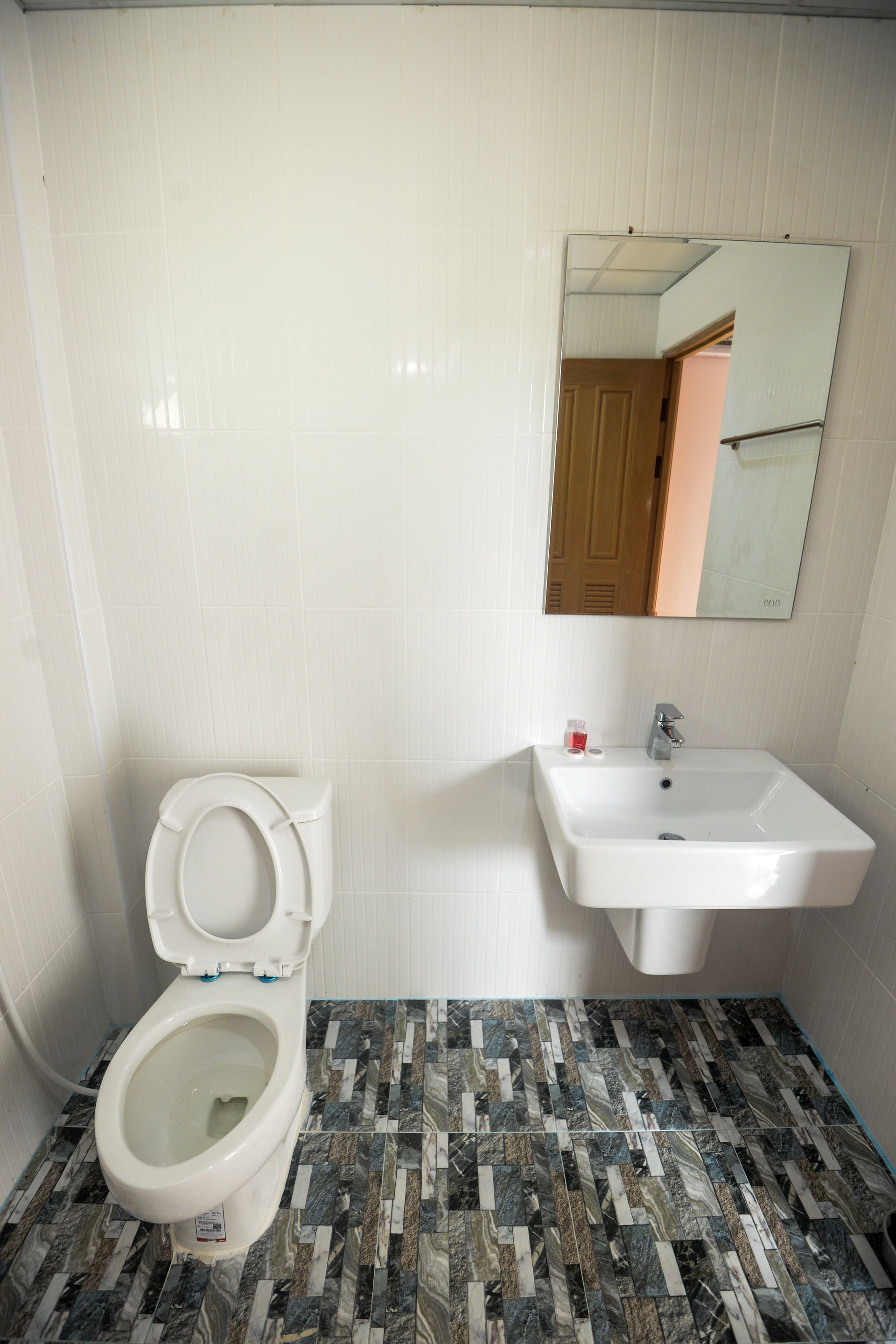 A bathroom with a toilet, sink, mirror, and patterned floor tiles.
