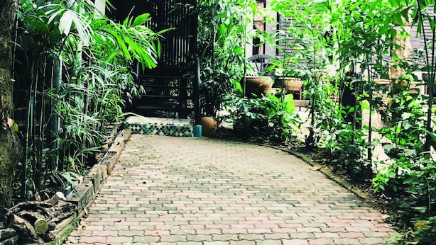 A paved pathway surrounded by lush greenery and a rustic building with a tiled entrance. - 339 Hotels & Resort (Nakhon Ratchasima)