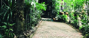 A paved pathway surrounded by lush greenery and a rustic building with a tiled entrance. - 339 Hotels & Resort (Nakhon Ratchasima)
