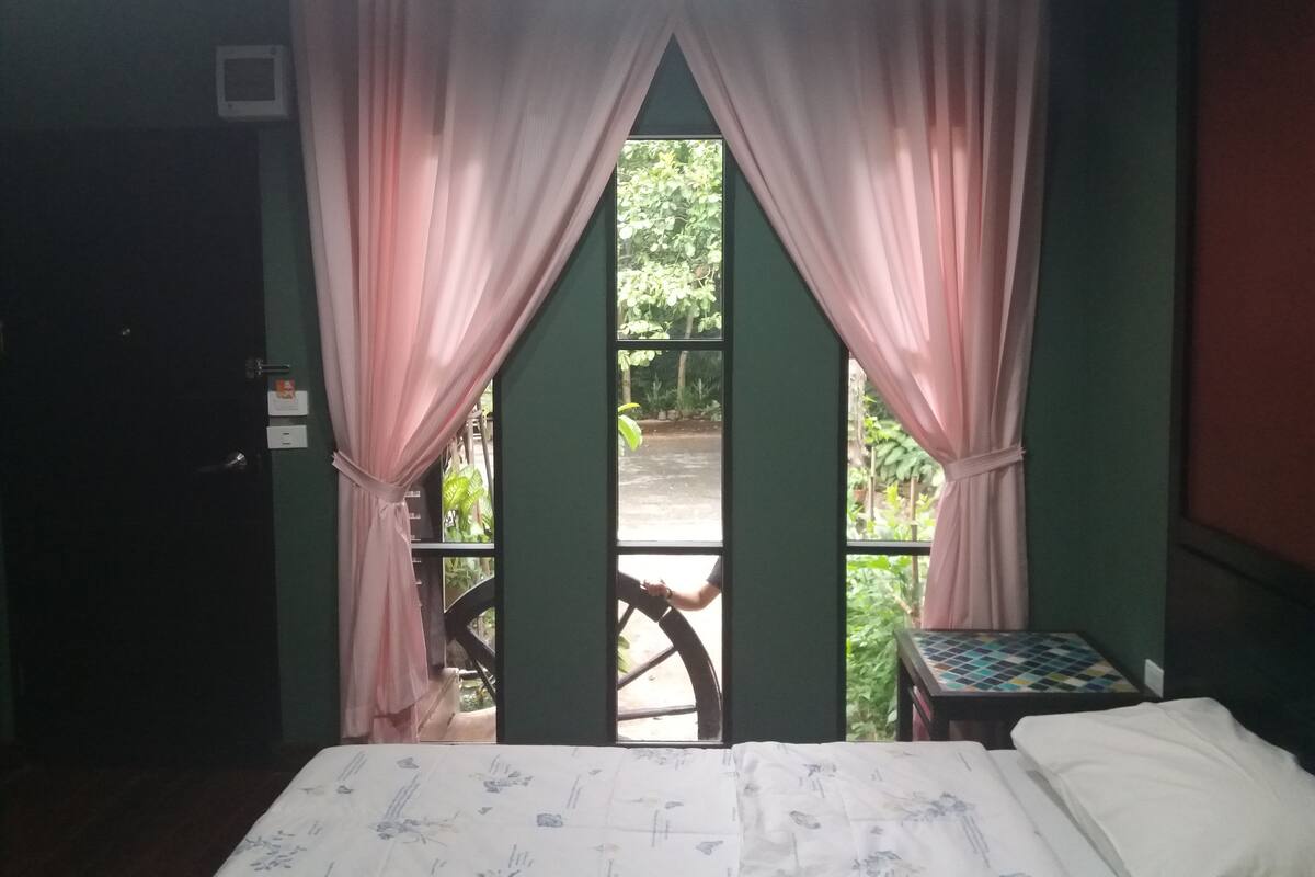 A room with a bed, a small table, and a window with pink curtains.