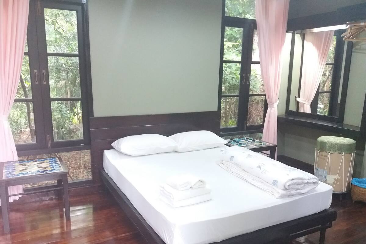 A neatly made bed with white linens and pillows, a wooden headboard, and a small table with a tiled top beside the bed.