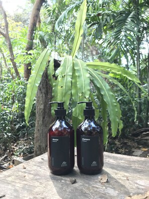 Two dark-colored bottles labeled 'shower' and 'shampoo' placed on a wooden surface with a tree and foliage in the background.