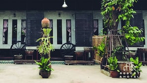 A courtyard with potted plants, a water wheel, and a building with black shutters. - 339 Hotels & Resort (Nakhon Ratchasima)