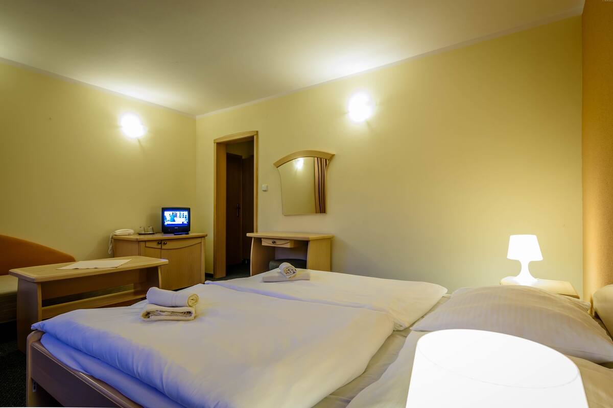 Quarto de hotel com cama, escrivaninha com computador, espelho e luminária.