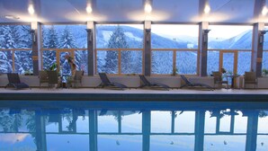 A pool area with lounge chairs and large windows offering a view of snow-covered mountains. - Hotel Boboty (Terchova)