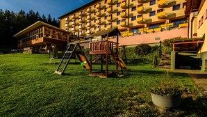 A large building with multiple balconies, a wooden play structure, and a grassy area. - Hotel Boboty (Terchova)