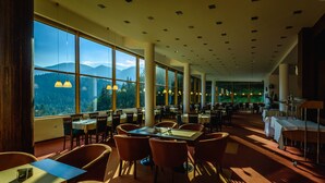 A spacious dining area with large windows offering mountain views, multiple tables and chairs, and pendant lighting. - Hotel Boboty (Terchova)
