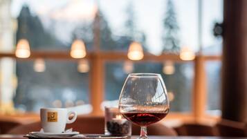 Una mesa con una copa de vino y una taza, una vela, y una vista de un paisaje nevado a través de amplias ventanas.