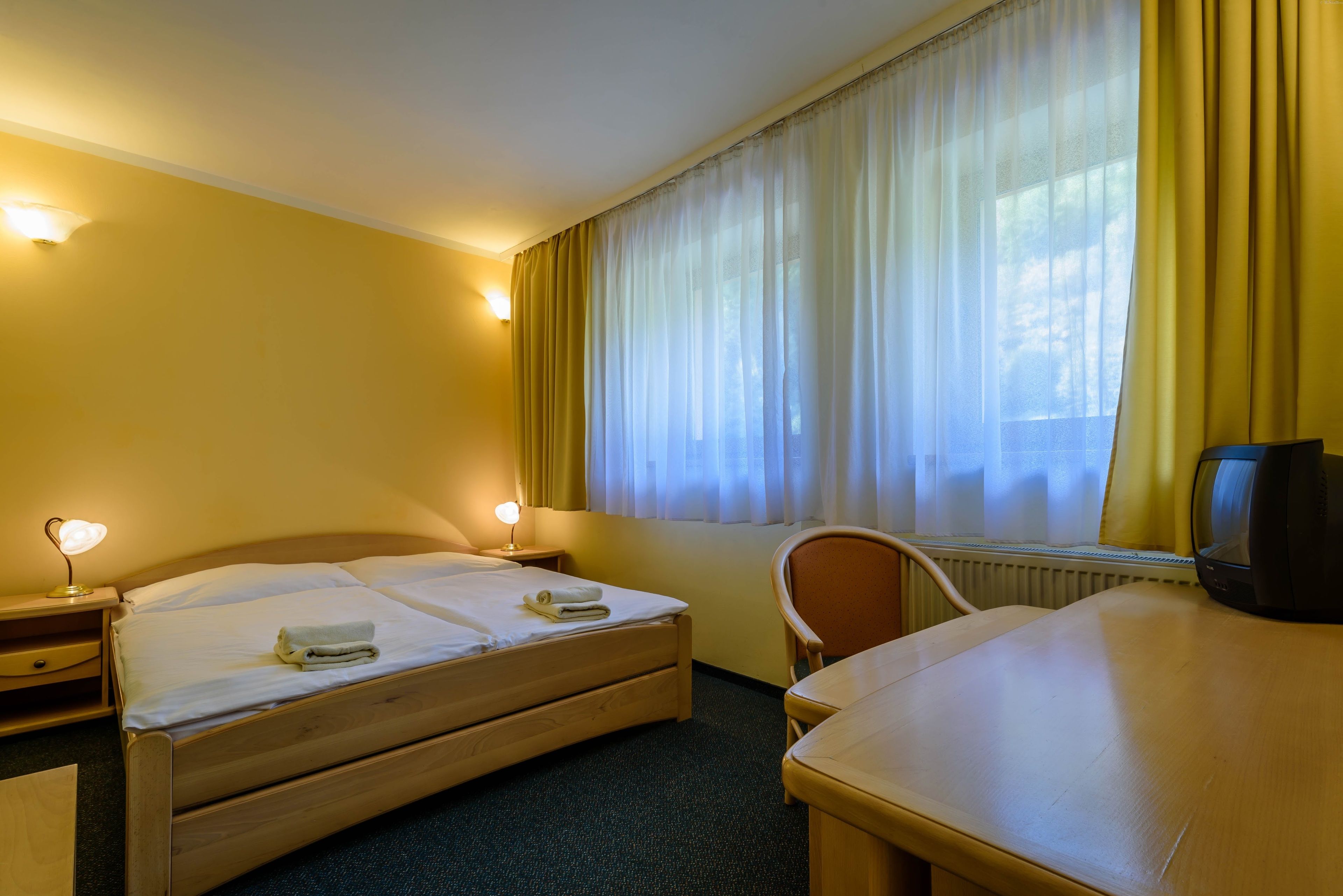Ein Hotelzimmer mit zwei Einzelbetten, einem Holztisch, einem Stuhl, einem Fernseher und einem Fenster mit Vorhängen.