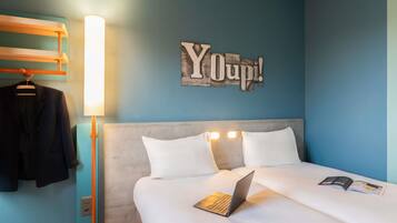 Une chambre d’hôtel avec un lit, un ordinateur portable, une lampe, un porte-manteau et un panneau mural.