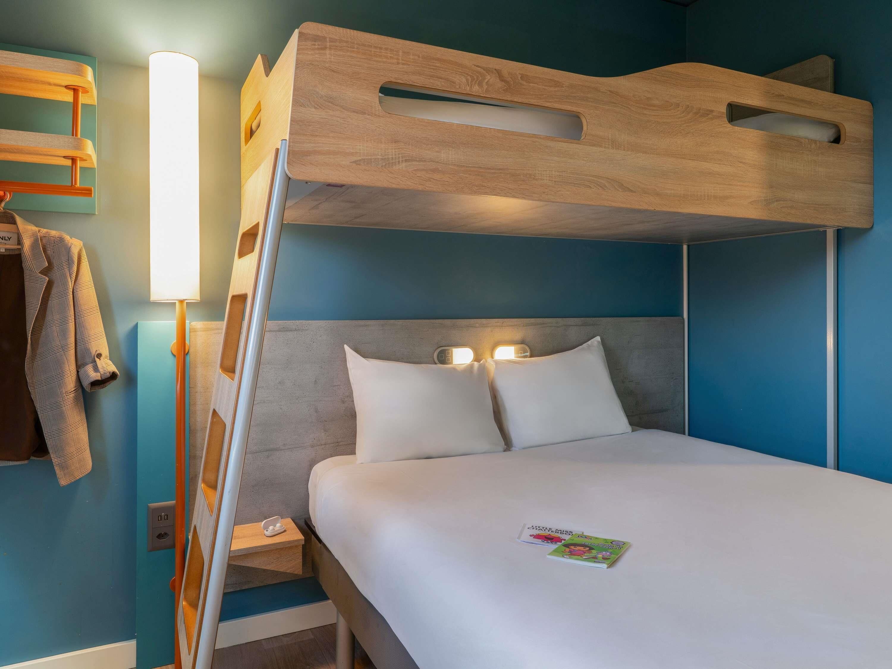 A bunk bed with a wooden headboard, a bedside table with a lamp, and a wall-mounted shelf with a jacket.