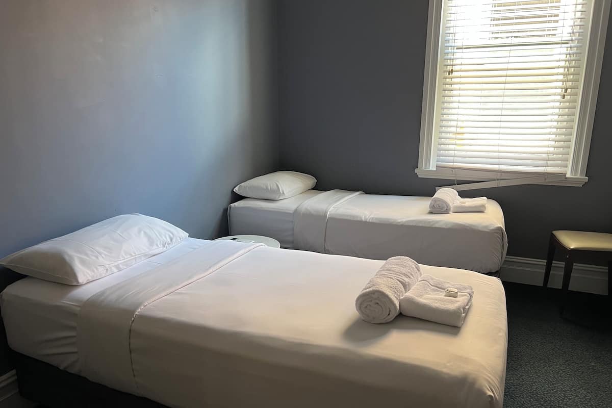 A hotel room with two single beds, a small round table, and a window with blinds.