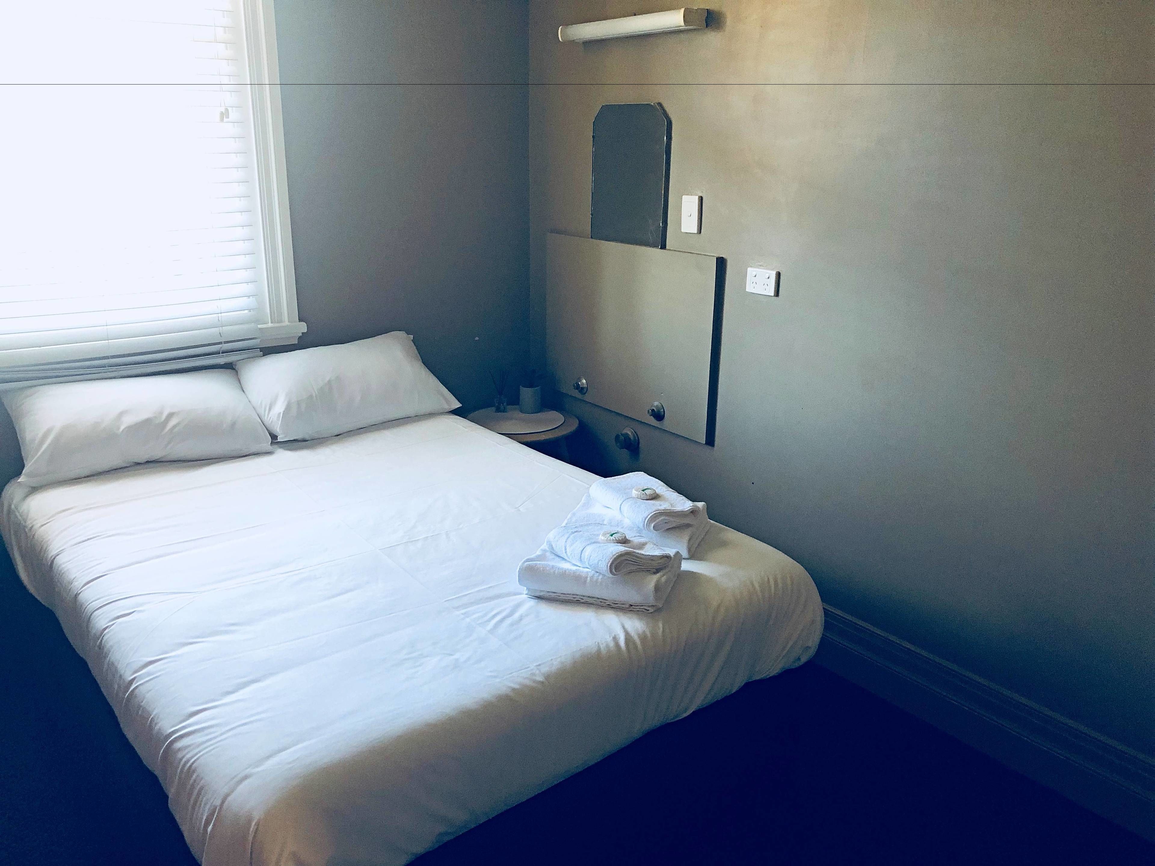 A neatly made bed with white linens, a bedside table with a lamp, and a wall-mounted mirror.