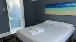 A hotel room with a bed, a painting of a beach, a bathroom with blue tiles, and a patterned floor. - Swansea Hotel (Swansea)
