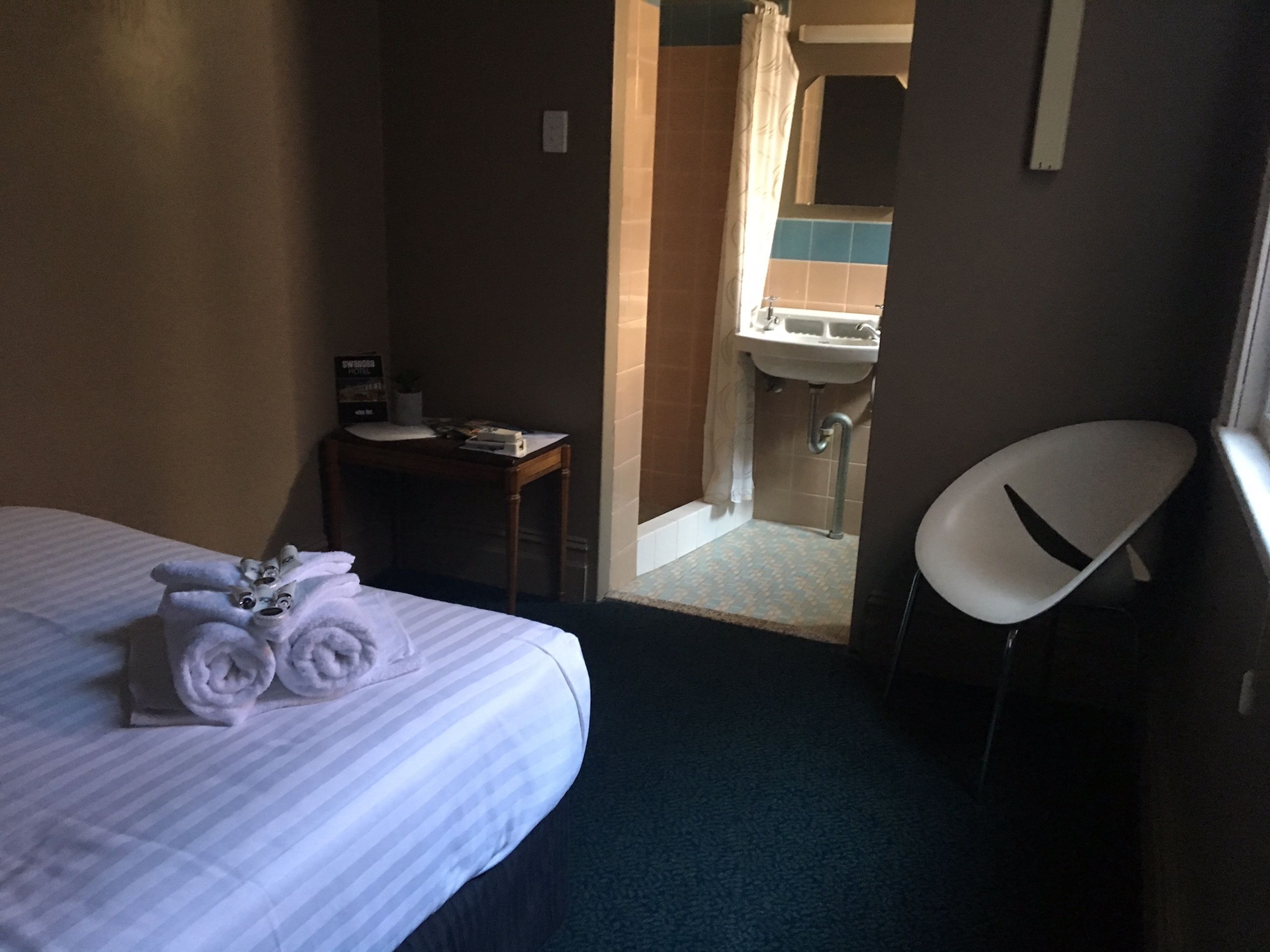 A hotel room with a bed, a desk, a chair, and a bathroom visible through an open door.