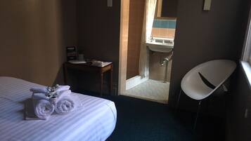 A hotel room with a bed, a desk, a chair, and a bathroom visible through an open door.