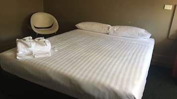 A hotel room with a neatly made bed, a round chair, and a white pillow.