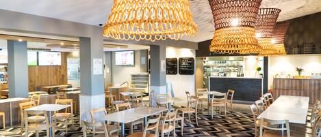 A modern restaurant with wooden tables and chairs, a patterned floor, and hanging wicker chandeliers.