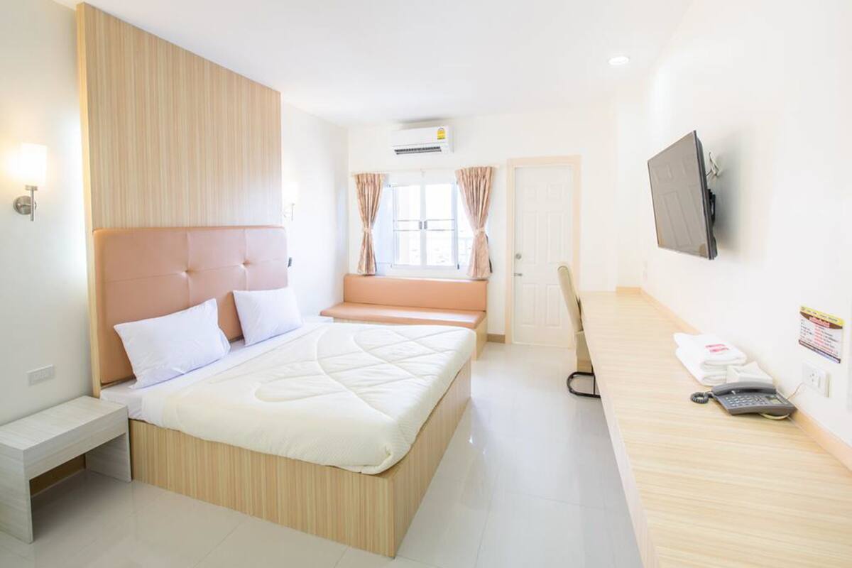 A hotel room with a large bed, a bedside table, a TV mounted on the wall, and a window with curtains.
