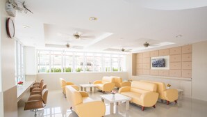 A modern hotel lobby with a seating area, a reception desk, and a large window offering a view of the outdoors. - P.A. Thani Hotel (Nakhon Sawan)