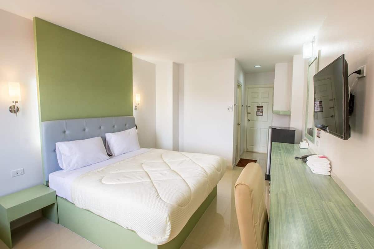 A hotel room with a bed, bedside table, chair, and a TV mounted on the wall.