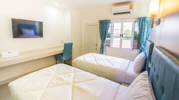 A hotel room with two beds, a desk, a chair, a TV, and an air conditioning unit.