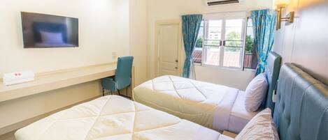 A hotel room with two beds, a desk, a chair, a TV, and an air conditioning unit.