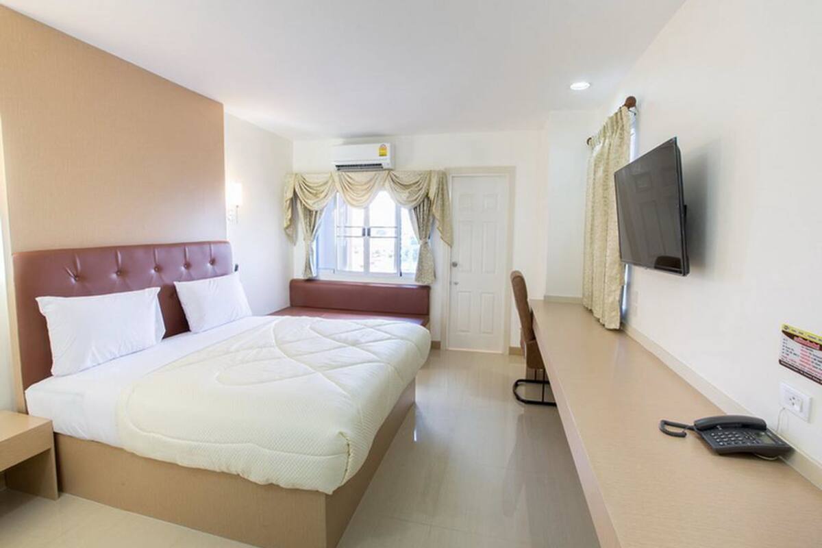 A hotel room with a bed, a TV, a desk, and a telephone.