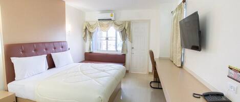 Habitación de hotel con una cama grande, un televisor montado en la pared, un escritorio con teléfono y una ventana con cortinas.