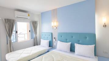 A hotel room with two beds, a window with curtains, an air conditioning unit, and wall-mounted lighting.