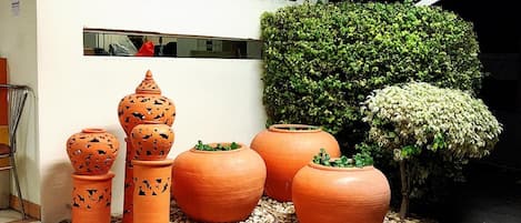 A hotel entrance with a sign in multiple languages, decorative pots, and a well-maintained hedge.