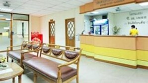 A reception area with a reception desk, seating area with chairs and a table, and a wall with a sign. - P.A. Place Hotel (Nakhon Sawan)