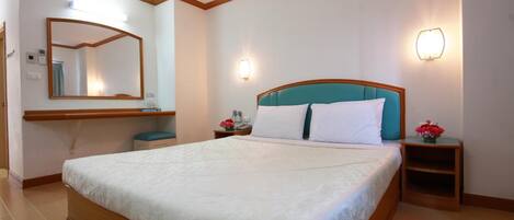 A neatly arranged bedroom with a large bed, a bedside table with a lamp, a mirror, and a wall-mounted light fixture.