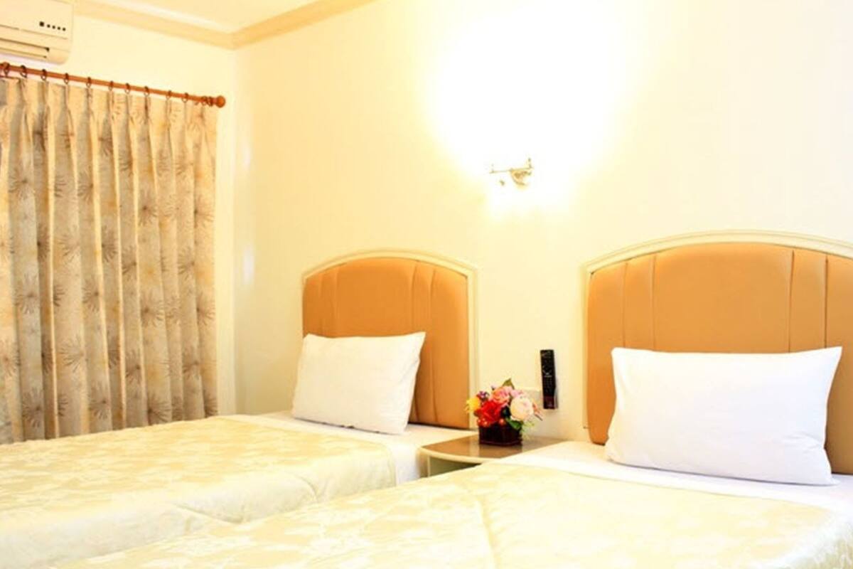 A hotel room with two beds, a nightstand with a vase of flowers, and a wall-mounted light fixture.