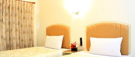 Habitación de hotel con dos camas, una mesita de noche con un florero y una lámpara fijada a la pared.