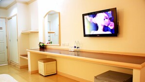 A hotel room with a wooden vanity, a mirror, a television mounted on the wall, a small trash bin, and a bed with a white mattress. - P.A. Ville Hotel (Nakhon Sawan)