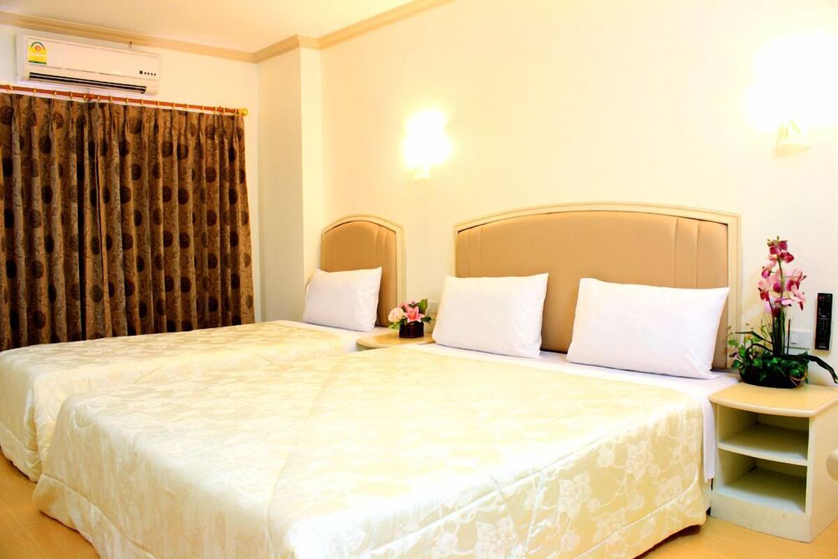 A double bed with a beige headboard, white bedding, and a nightstand with a vase of flowers.