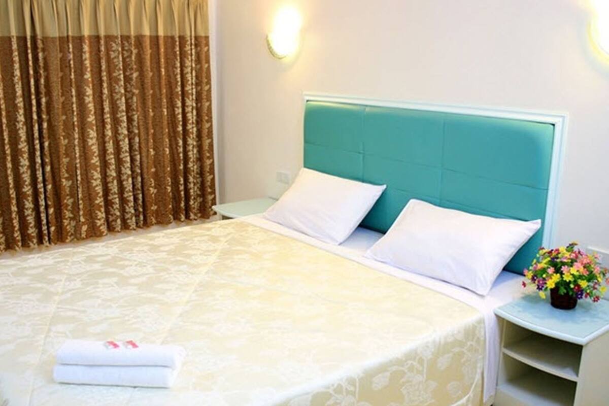 A neatly made bed with white linens, a teal headboard, and a small bedside table with a vase of flowers.