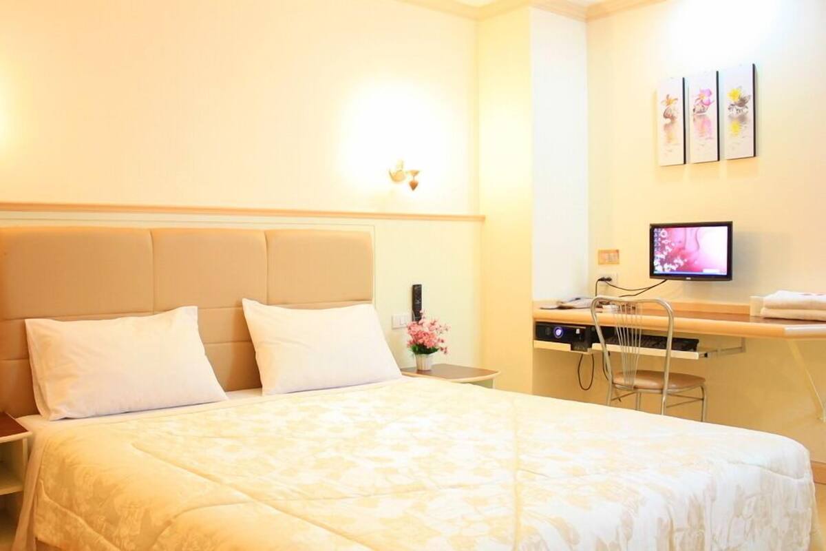 A hotel room with a bed, bedside tables, a desk with a computer, and wall-mounted artwork.
