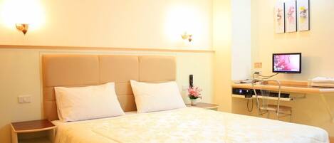 A hotel room with a bed, bedside tables, a desk with a computer, and wall-mounted artwork.