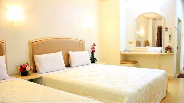 A hotel room with two beds, a bedside table with a vase of flowers, a mirror above the sink, and a towel rack. - P.A. Ville Hotel (Nakhon Sawan)