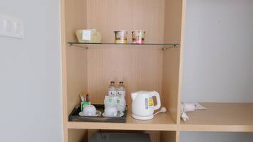 A compact kitchenette with a small refrigerator, a coffee maker, and a kettle on the countertop.
