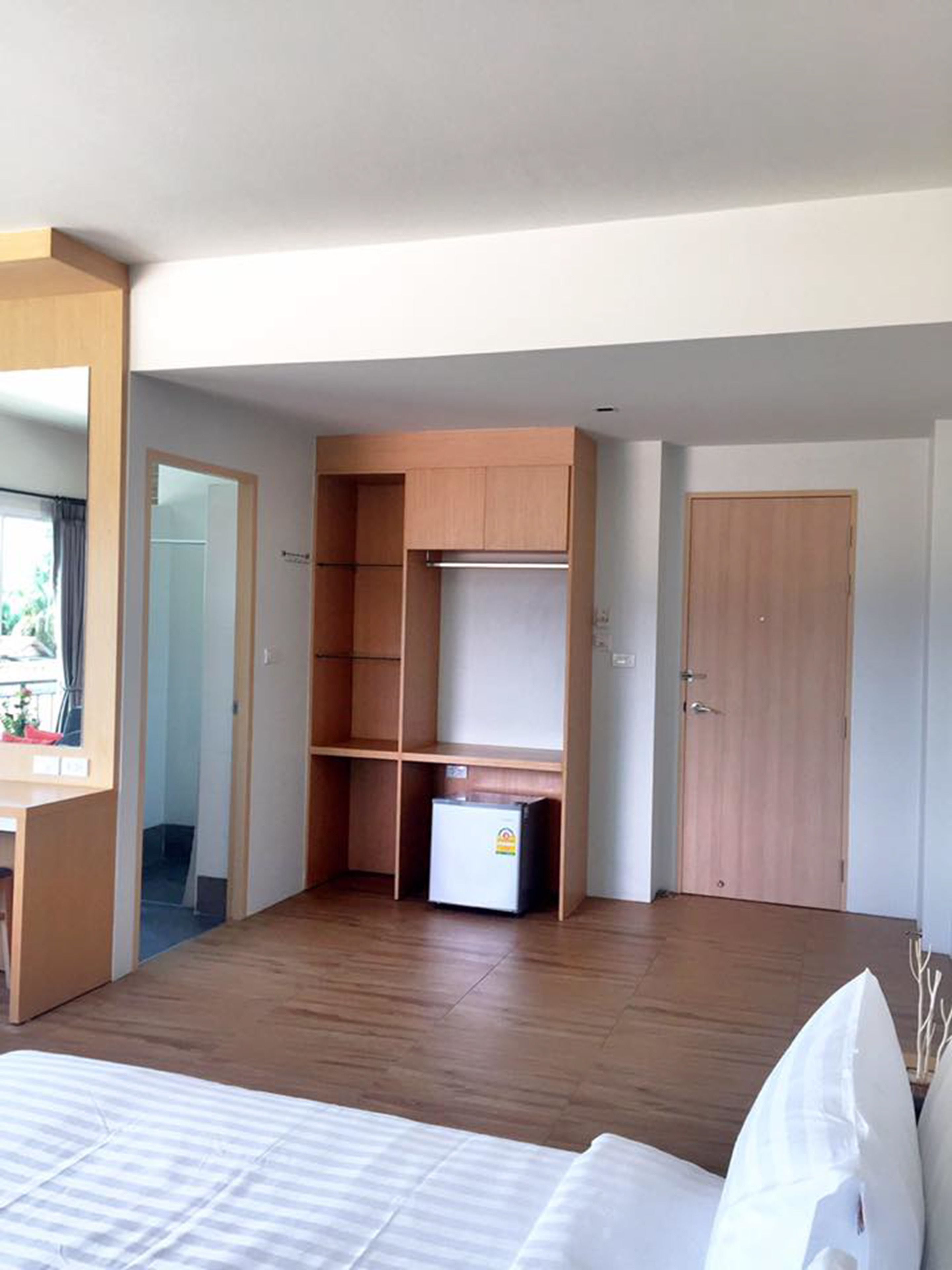 A bedroom with a bed, wooden wardrobe, and a small refrigerator.