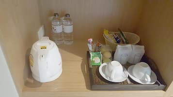 A kitchenette with a coffee maker, two bottles of water, a basket with snacks, and a tray with cups and a teapot.