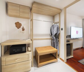 Una habitación moderna con un escritorio de madera, una mesita pequeña, un televisor y una bata colgada en un perchero.
