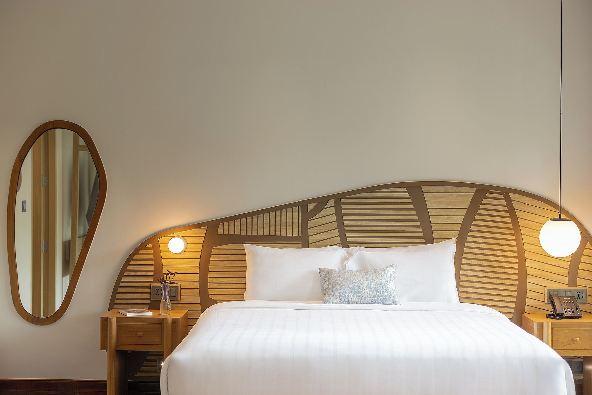 Una cama bien hecha con cabecera de madera, dos mesitas de noche con lámparas y un espejo grande en la pared.
