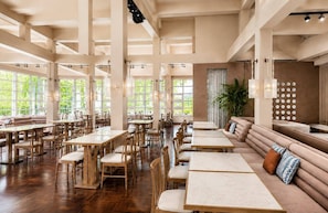 Un restaurante espacioso con techos altos, ventanas amplias y una combinación de mesas y zonas de estar de madera.