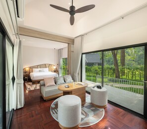 Un dormitorio moderno con una cama grande, un sofá, una mesa de centro y un balcón con vistas al verdor.
