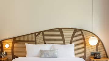 Une chambre d’hôtel avec une tête de lit incurvée, un lit avec une literie blanche, une table de chevet avec une lampe et un téléphone sur la table de nuit.